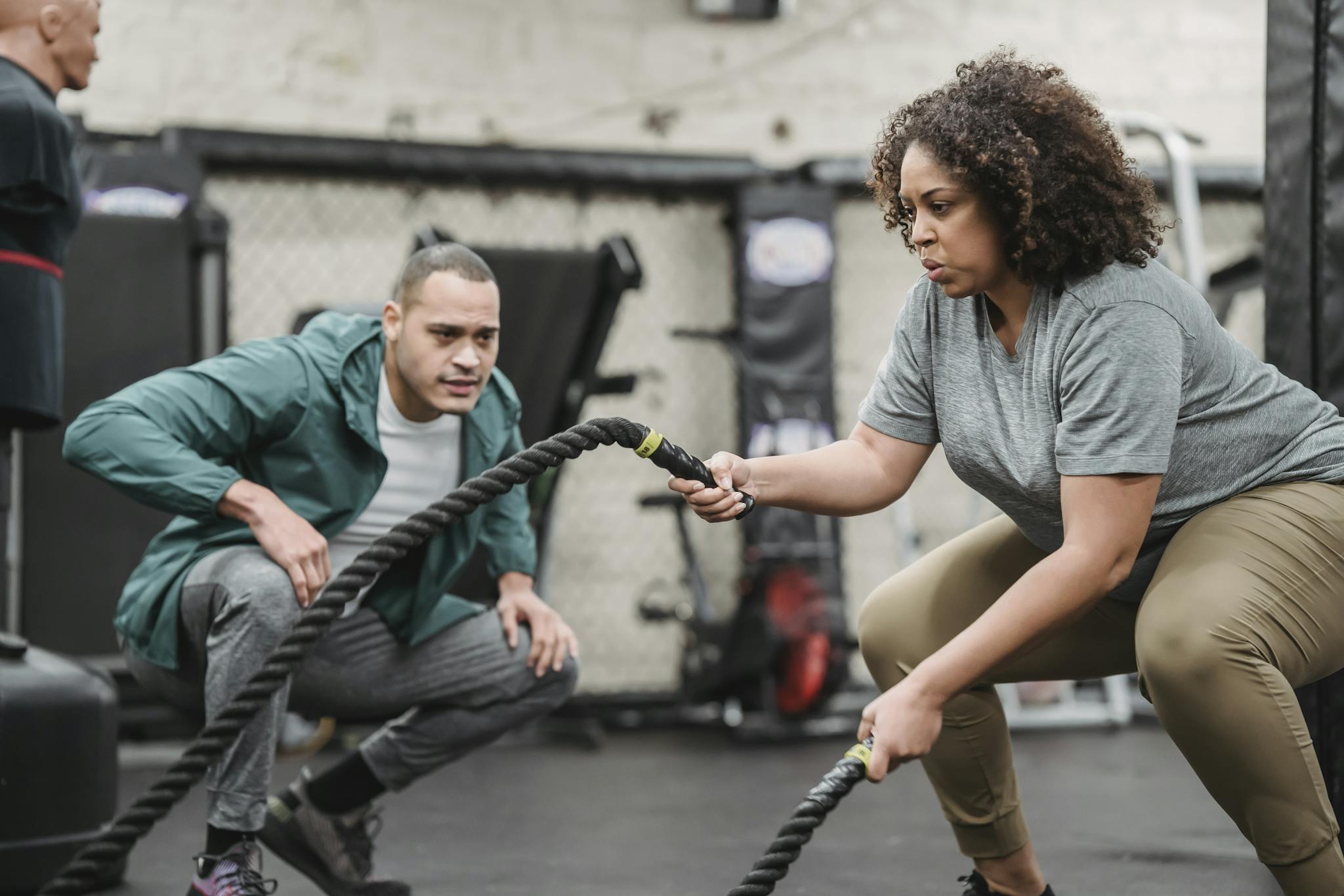 Determined black plump woman exercising with battle ropes in gym